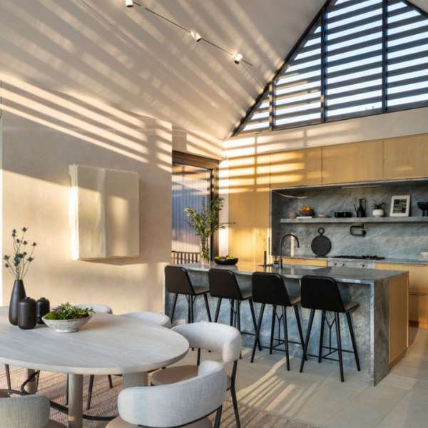 Bright living room with floor-to-ceiling patio doors and expansive windows and doors, featuring a vaulted ceiling, modern neutral furniture, and a view of a lush green garden, emphasizing the natural light and airy connection provided by stylish patio doors.
