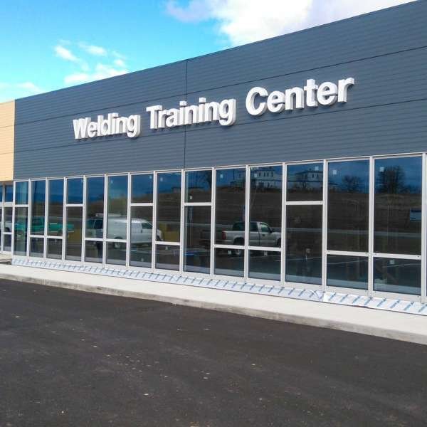Modern grey welding training center building with large windows, situated in a commercial real estate property.