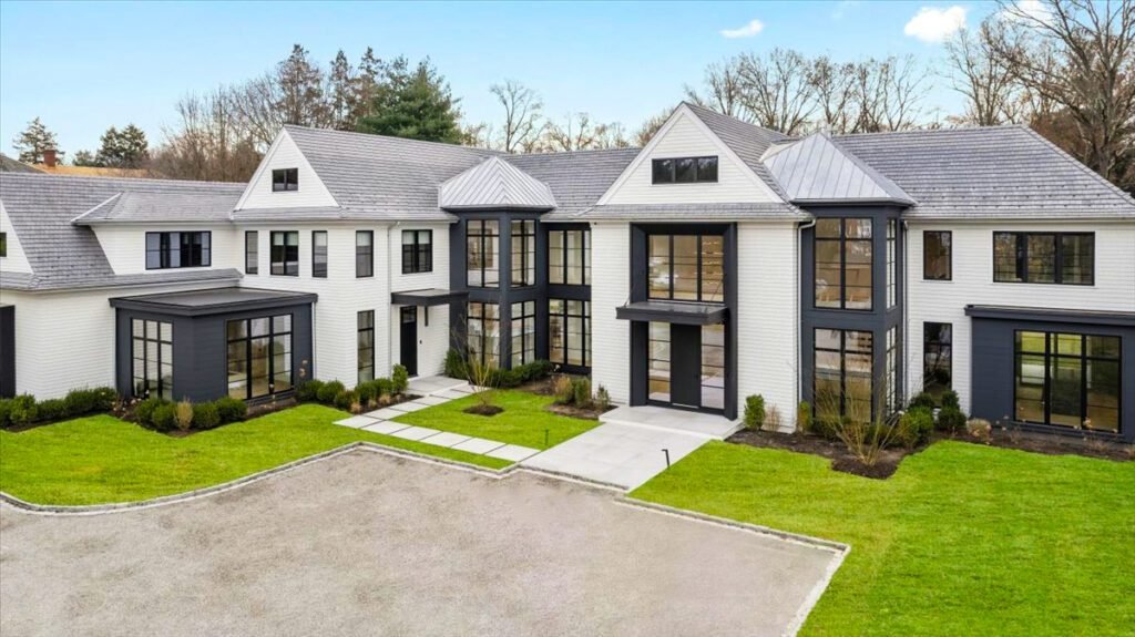 modern, luxury two-story home featuring large, black-framed European-style windows and sleek entry doors. The architectural design emphasizes symmetry, clean lines, and ample natural light through expansive glass surfaces. The windows are likely energy-efficient and custom-fitted, enhancing both curb appeal and performance. The front door and secondary entry doors appear to be minimalist and well-integrated into the overall design.