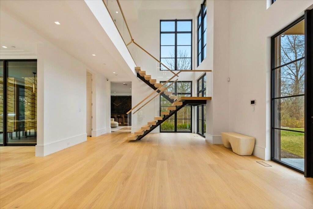 A modern living room with large black-framed European windows installed beneath a staircase. The windows bring in natural light, enhancing the open-concept space and highlighting the architectural detail of the stairs above. Expertly installed for both aesthetic appeal and energy efficiency.
