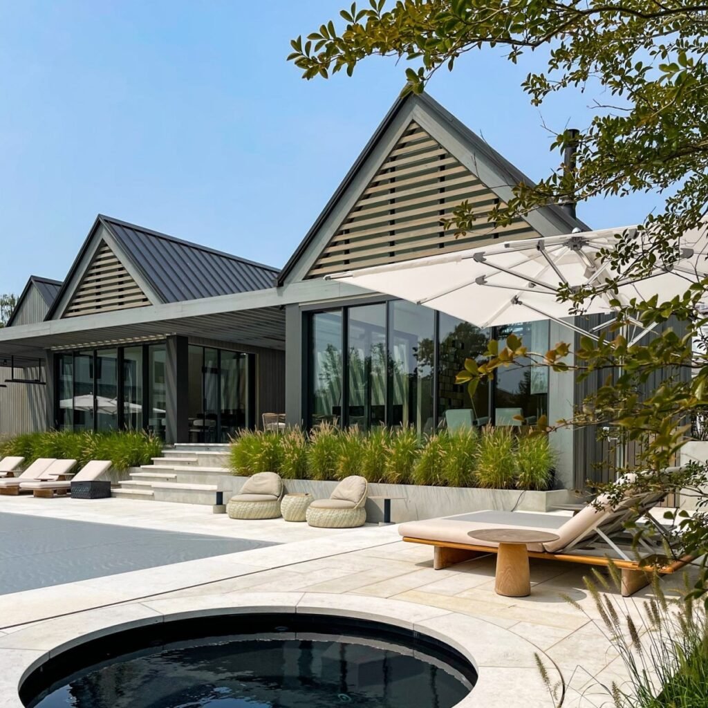 Modern home exterior featuring large sliding glass windows and doors, framed in sleek black metal, opening onto a minimalist patio with concrete steps, outdoor seating, and lush green landscaping—highlighting the seamless connection between indoor and outdoor spaces through contemporary windows and doors.