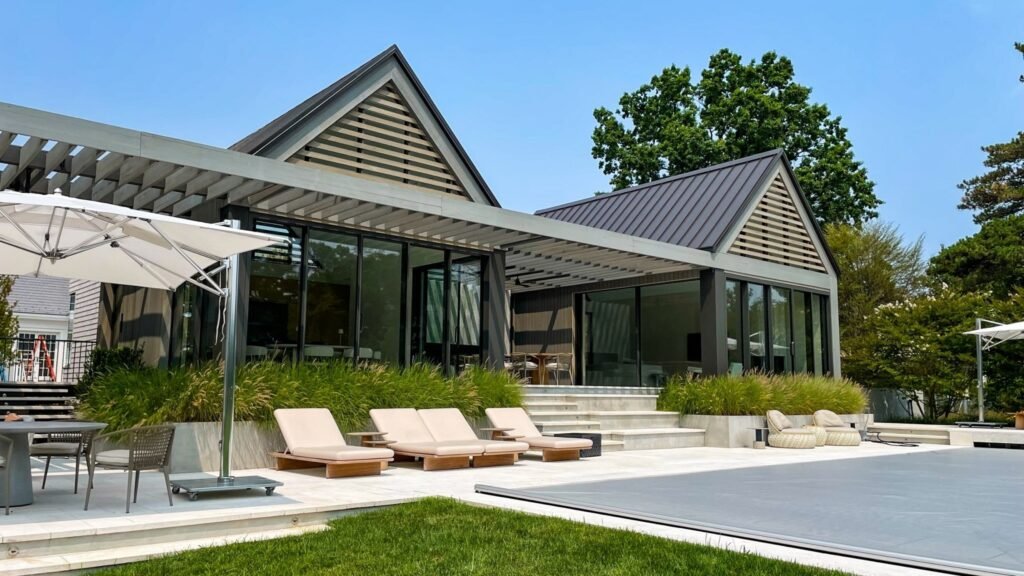 Modern home exterior featuring large sliding glass windows and doors, framed in sleek black metal, opening onto a minimalist patio with concrete steps, outdoor seating, and lush green landscaping—highlighting the seamless connection between indoor and outdoor spaces through contemporary windows and doors.