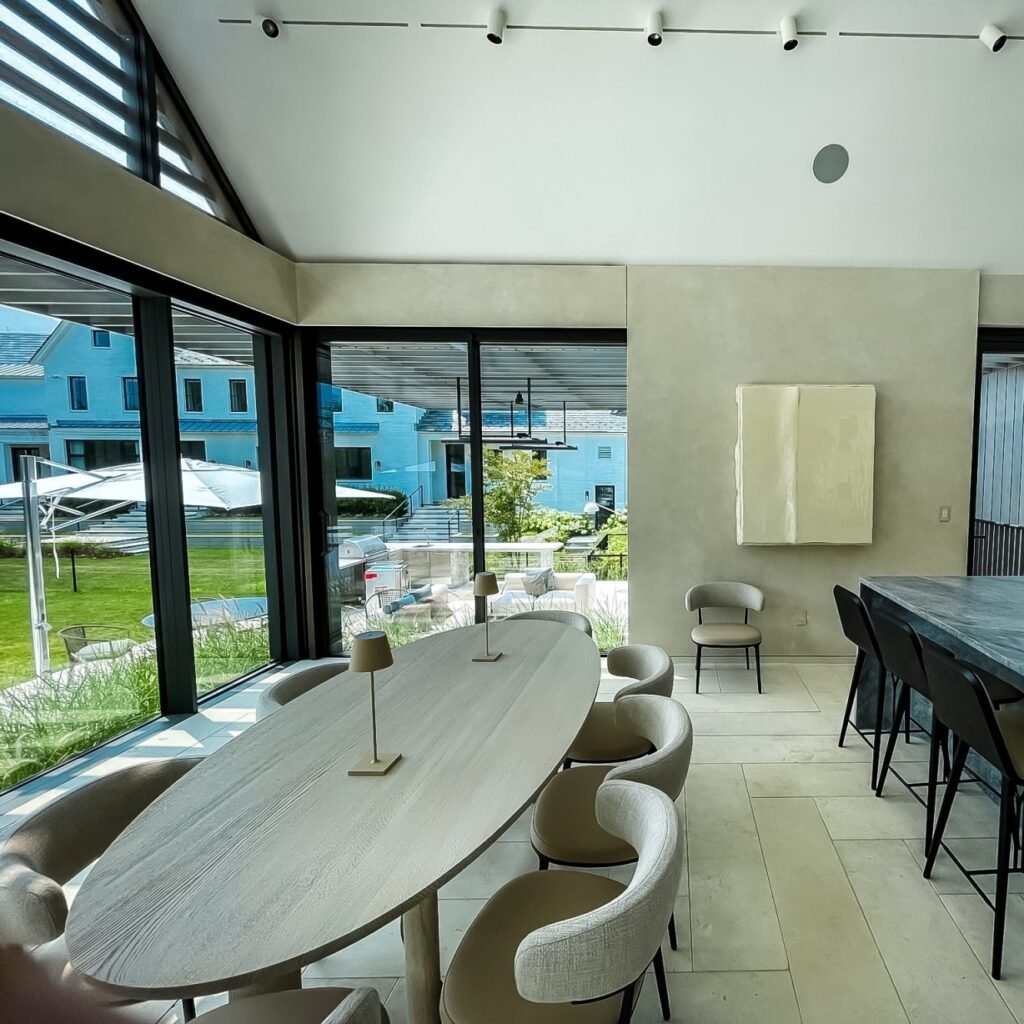 Modern home exterior featuring large sliding glass windows and doors, framed in sleek black metal, opening onto a minimalist patio with concrete steps, outdoor seating, and lush green landscaping—highlighting the seamless connection between indoor and outdoor spaces through contemporary windows and doors.
