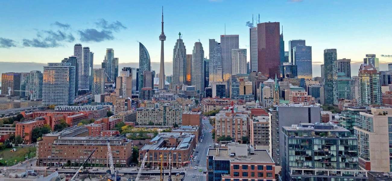 Toronto city skyline featuring the CN Tower, modern skyscrapers, and Lake Ontario on a clear sunny day.